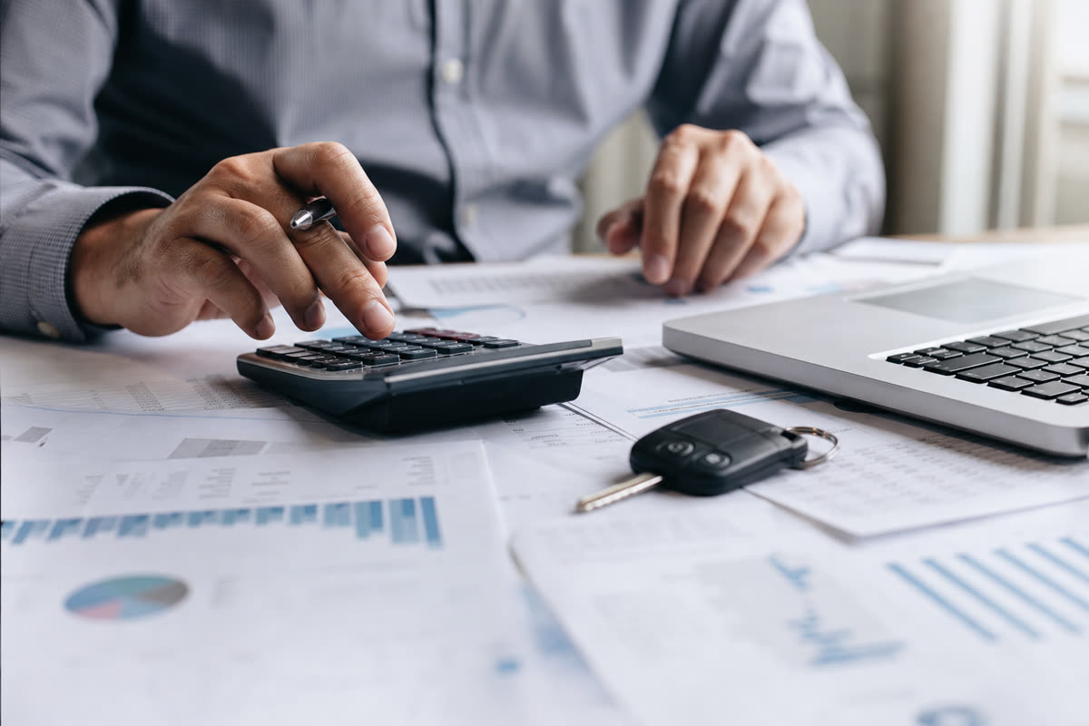 Продавец считает налог с продажи машины на калькуляторе рядом с документами и ноутбуком